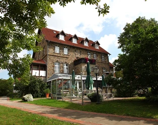 Außenansicht Landhaus Schieder Dreistöckiges, steinernes Landhaus mit rotem Dach, Wintergarten, umgeben von gepflegten Bäumen.