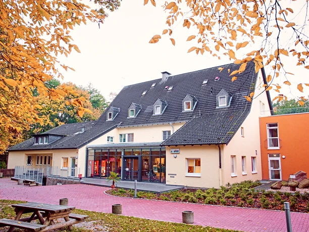 Jugendherberge mit mehrstöckigem Gebäude, großem Glasfoyer und Herbstlaub im Vordergrund.