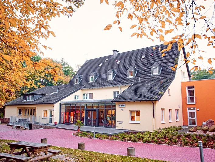 DJH Detmold - Außenansicht Jugendherberge mit mehrstöckigem Gebäude, großem Glasfoyer und Herbstlaub im Vordergrund.