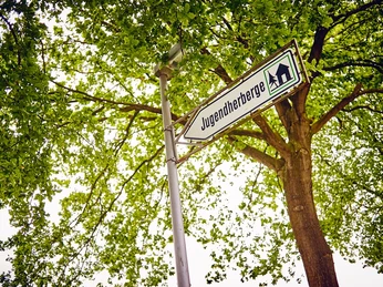 DJH Detmold - Wegweiser Wegweiser zu einer Jugendherberge, im Vordergrund ein Straßenschild, von Bäumen umgeben.