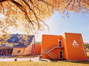 DJH Detmold - Außenansicht Die DJH Jugendherberge Detmold in herbstlicher Kulisse; oranges Gebäude mit Laub im Vordergrund.