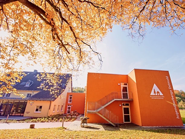 DJH Detmold - Außenansicht Die DJH Jugendherberge Detmold in herbstlicher Kulisse; oranges Gebäude mit Laub im Vordergrund.
