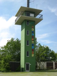 Panoramaerlebnisturm Hohe Asch Grüner Aussichtsturm mit sechs Stockwerken, farbenfrohen Motiven an der Front und umliegendem Grün.