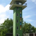 Panoramaerlebnisturm Hohe Asch Grüner Aussichtsturm mit sechs Stockwerken, farbenfrohen Motiven an der Front und umliegendem Grün.