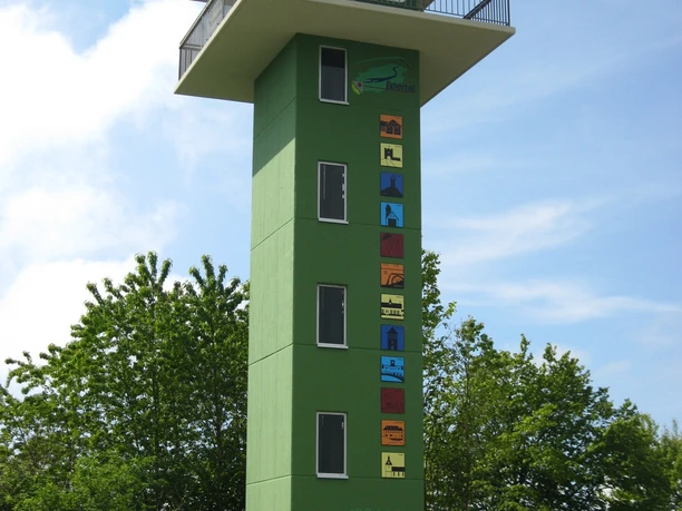 Panoramaerlebnisturm Hohe Asch Grüner Aussichtsturm mit sechs Stockwerken, farbenfrohen Motiven an der Front und umliegendem Grün.