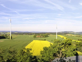 Blick von der Aussichtsplattform Richtung Westen Weitsichtige Aussicht über grüne Felder mit vereinzelten Windrädern unter klarem blauen Himmel.