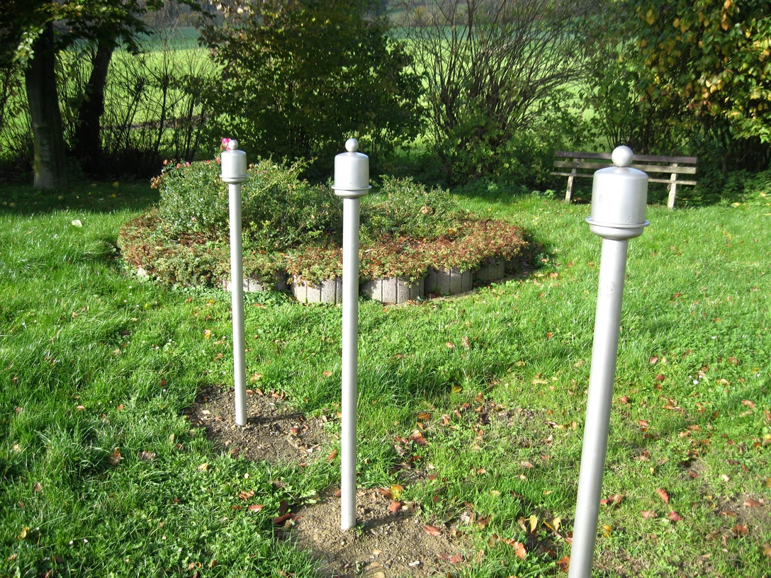 Duftorgel in Extertal-Kükenbruch Drei weiße Duftstelen im Grünen, umgeben von Büschen und Bäumen, nahe einer Holzbank im Park.