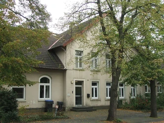 Ehemalige Kantorschule mit heller Fassade, flankiert von grünen Bäumen an einer ruhigen Straße.