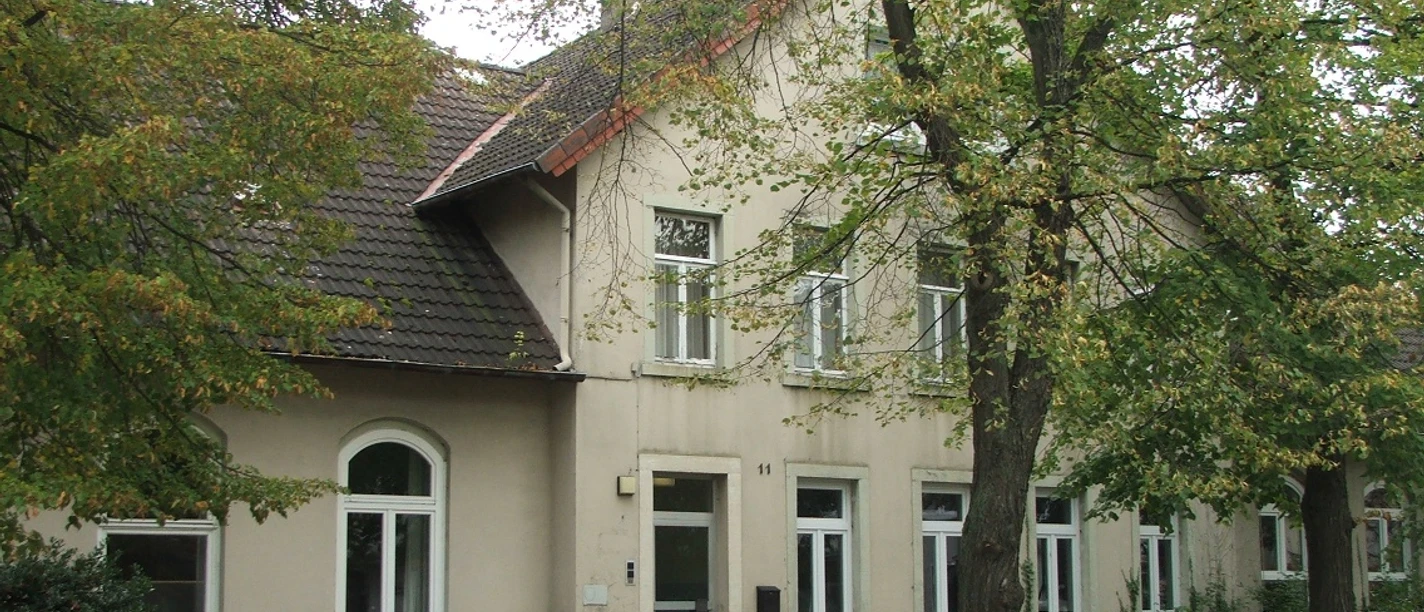 Ehemalige Kantorschule mit heller Fassade, flankiert von grünen Bäumen an einer ruhigen Straße.