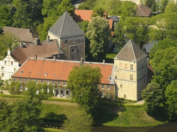 Schloss Rheda Luftaufnahme einer historischen Burganlage umgeben von grünen Bäumen und einem kleinen Fluss.