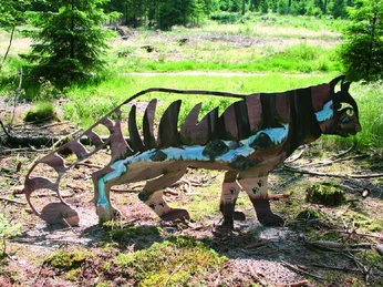 Katzen-Augen-Blicke Ein farbenfrohes Katzenkunstwerk steht im Wald, umgeben von grüner Vegetation und Sonnenlicht.