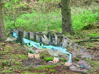 Katzen-Augen-Blicke Metallskulptur einer Katze mit großen, grünen Augen im Wald auf moosigem Boden zwischen Bäumen.