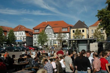 Neustadtmarktplatz Menschen versammeln sich auf einem belebten Marktplatz mit Fachwerkhäusern und Tischen unter freiem Himmel.