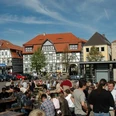 Neustadtmarktplatz Menschen versammeln sich auf einem belebten Marktplatz mit Fachwerkhäusern und Tischen unter freiem Himmel.