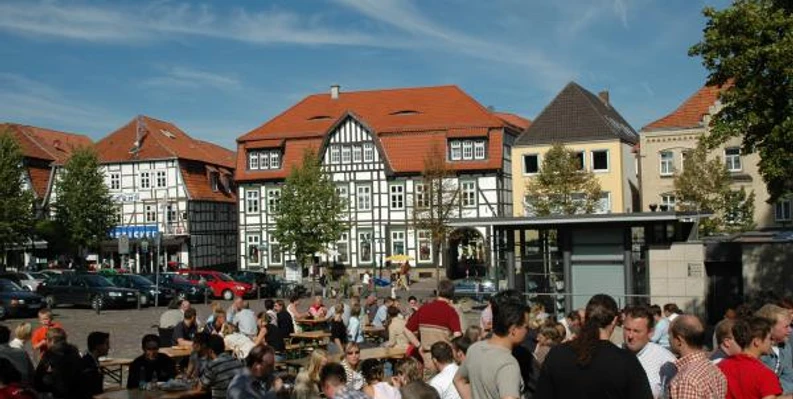 Neustadtmarktplatz Menschen versammeln sich auf einem belebten Marktplatz mit Fachwerkhäusern und Tischen unter freiem Himmel.