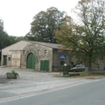 Steinernes Bauernhaus mit großen Toren, von Bäumen umgeben, an einer ruhigen Landstraße gelegen.