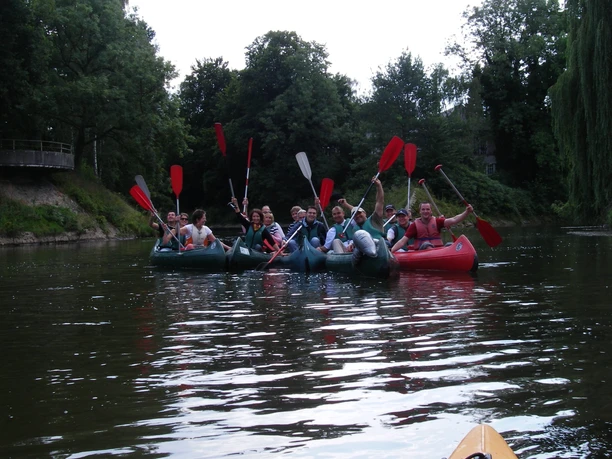 Menschen paddeln in mehreren Kanus eine friedliche Flusslandschaft entlang, umgeben von Bäumen.