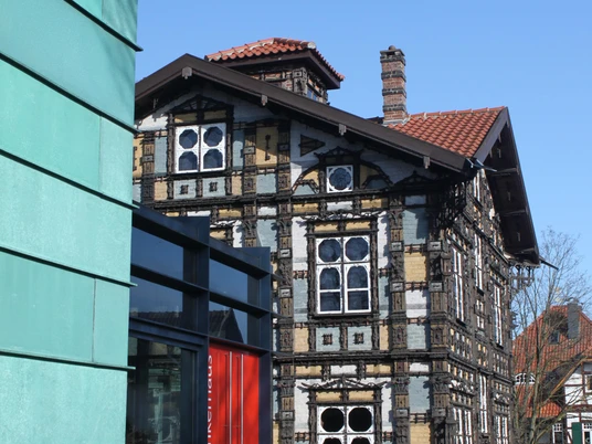 Fachwerkhaus mit kunstvoll verzierten Fassaden und rotem Eingangsbereich unter blauem Himmel.