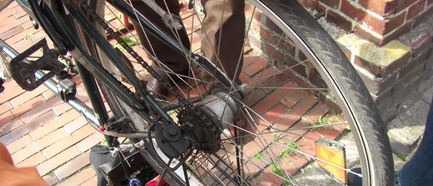 Fahrradfachgeschäft Zwei Personen reparieren gemeinsam ein Fahrradlaufrad auf einem Pflasterweg neben einer Backsteinmauer.