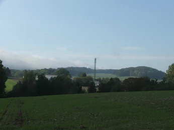 Blick von der Egge Landwirtschaftliche Fläche mit grünen Wiesen und einem entfernten Bohrturm unter einem blauen Himmel.