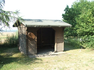 Holzhütte mit grünem Dach in grüner Umgebung; schattiger Innenraum Schutz bei Wanderungen.