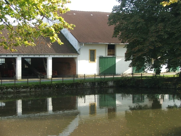 Gut Stapelage Gut Stapelage liegt an einem Teich, umgeben von Bäumen. Die Gebäude haben rote Ziegeldächer.