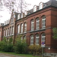 Bürgerschule Backsteinbau der Bürgerschule mit vielen Fenstern und Dachgauben, umgeben von Bäumen und Herbstlaub.