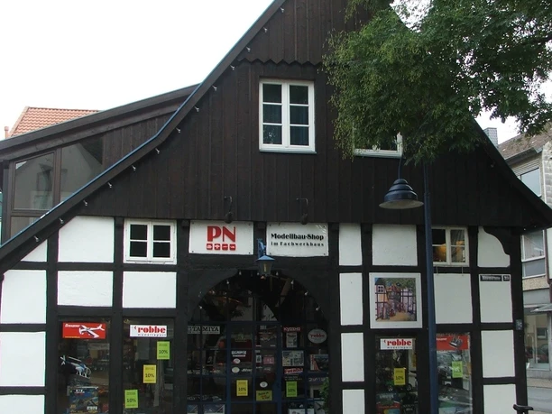 Fachwerkhaus mit weißem Putz und dunklen Holzbalken, Geschäfte im Erdgeschoss, Kopfsteinpflaster davor.