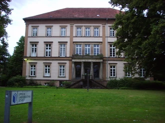 Lippische Landesbibliothek Historisches, helles Gebäude mit roten Dachziegeln, großen Fenstern und einer gepflegten Rasenfläche.