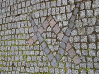 Mosaik in Pflastersteinen mit Kreuzsymbolen auf bemoostem Kopfsteinpflaster trotzt der Zeit.