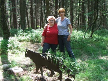 Ortrud Hinze, Karen Tank Zwei Frauen stehen nahe einer Metallskulptur eines Tigers in einem sonnigen Waldstück.