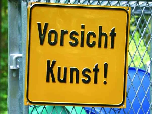 Mensch und Natur Gelbes Schild mit der Aufschrift "Vorsicht Kunst!" hängt an einem Zaun vor grüner Waldkulisse.