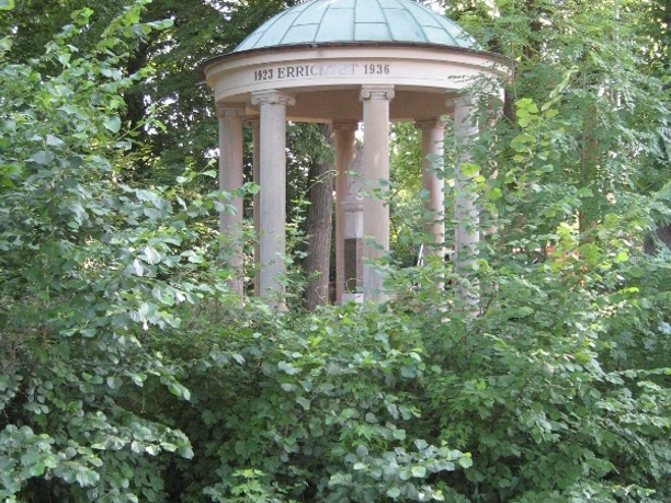 Gedenkstätte für die Gefallenen Ein klassizistischer Pavillon mit Säulen und Kuppeldach, umgeben von dichter, grüner Vegetation.