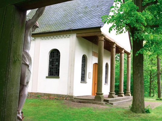 Rellerkapelle Kleine Kapelle mit Schindeldach und Glockenturm, umgeben von grünen Bäumen und Rasenfläche.