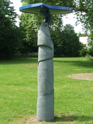Moderne Skulptur auf Rasenfläche, bestehend aus spiralförmiger Steinstruktur mit blauer Metallplatte oben.