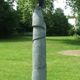 Regenwasserbaum Moderne Skulptur auf Rasenfläche, bestehend aus spiralförmiger Steinstruktur mit blauer Metallplatte oben.