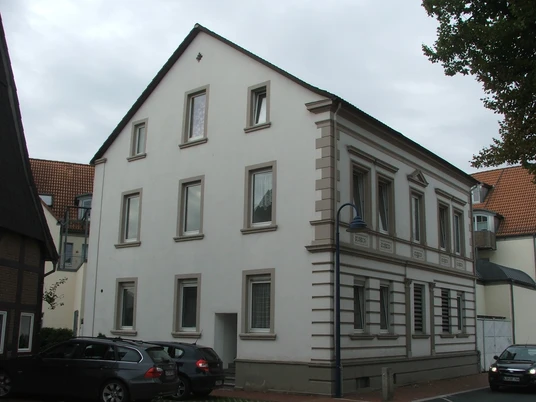 Haus Rhienstraße 30 Ein dreistöckiges weißes Wohnhaus aus dem 19. Jahrhundert mit markanten Fenstereinfassungen.