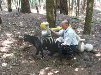 Wilhelm Wortberg Ein Mann in einem Wald sitzt nah bei einer Metallskulptur eines Höhlenlöwen und einem Knochen.