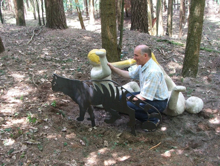 Wilhelm Wortberg Ein Mann in einem Wald sitzt nah bei einer Metallskulptur eines Höhlenlöwen und einem Knochen.
