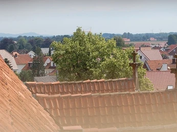 Blick vom Kirchturm Blick über rote Ziegeldächer und Kreuze in einer ländlichen, idyllischen Dorfszene mit bewölktem Himmel.
