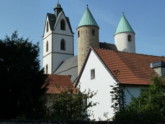 Die Busdorfkirche mit ihren zwei markanten Rundtürmen und rotem Ziegeldach bei strahlend blauem Himmel.
