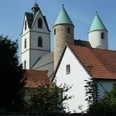 Die Busdorfkirche mit ihren zwei markanten Rundtürmen und rotem Ziegeldach bei strahlend blauem Himmel.