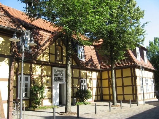 Altes Progymnasium Fachwerkhaus im Sonnenschein, von Bäumen umgeben, mit markanter weißer Türe und Straßenlaterne.