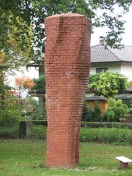 Stele im Friedenpark Backsteinstele im Park von Bäumen umgeben, symbolisiert Reflexion und Ruhe im öffentlichen Raum.