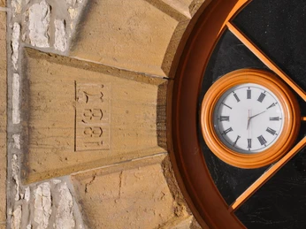 Detailansicht Rathaus Uhr in einem runden Fenster mit römischen Ziffern, umgeben von Sandsteinmauerwerk, zeigt 13:29 Uhr.