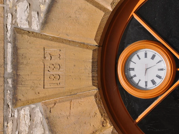 Detailansicht Rathaus Uhr in einem runden Fenster mit römischen Ziffern, umgeben von Sandsteinmauerwerk, zeigt 13:29 Uhr.
