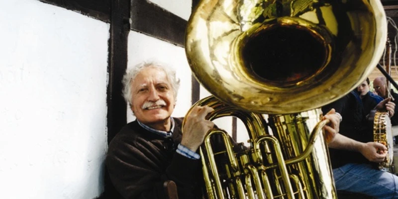 Musiker von nah und fern genießen die freundliche Atmosphäre im Jazzkotten Älterer Mann mit grauem Haar spielt eine glänzende Tuba und lächelt, traditionelle Fachwerkfassade im Hintergrund.