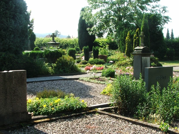 Friedhof Heiden Grünbewachsener Friedhof mit gepflegten Grabsteinen und Wegen, umgeben von Bäumen und Gebüschen.