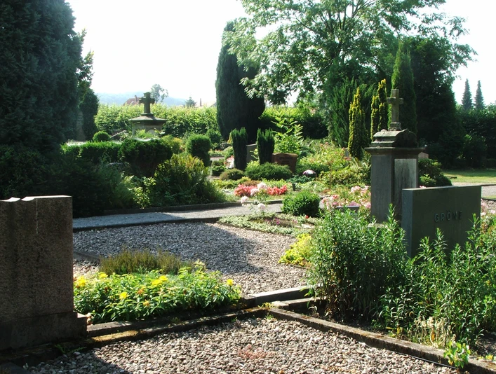 Friedhof Heiden Grünbewachsener Friedhof mit gepflegten Grabsteinen und Wegen, umgeben von Bäumen und Gebüschen.