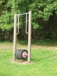 Ein Spielgerät mit Reifenrolle auf einem Rasenplatz, umgeben von dichter grüner Vegetation.